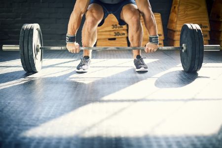Low section of muscular man lifting barbell in gym