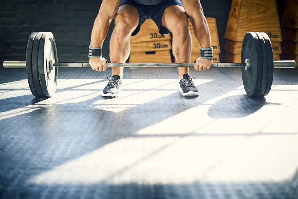 Low section of muscular man lifting barbell in gym
