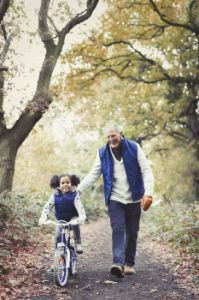 Grandfather and granddaughter bike riding on path in autumn park